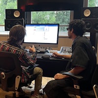 two people sitting at desks in a recording studio